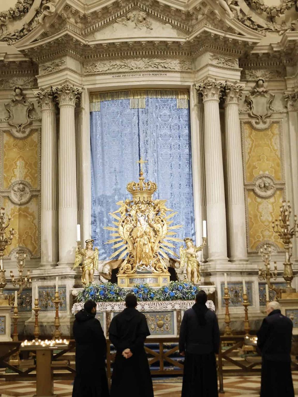 Immaculate church altar with ornate gold sculpture and blue drape, religious art, and worshippers.
