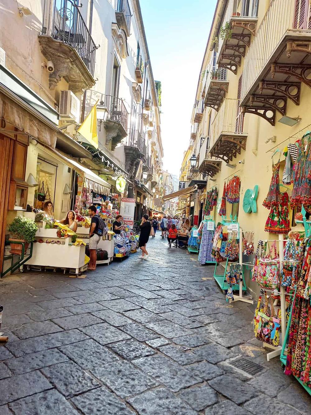 Vibrant street market in Italy, featuring colorful clothing and souvenir stalls on a sunny day.