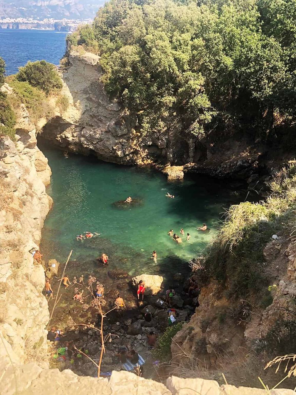 Secluded natural swimming hole with clear turquoise water surrounded by rocky cliffs and lush greenery.