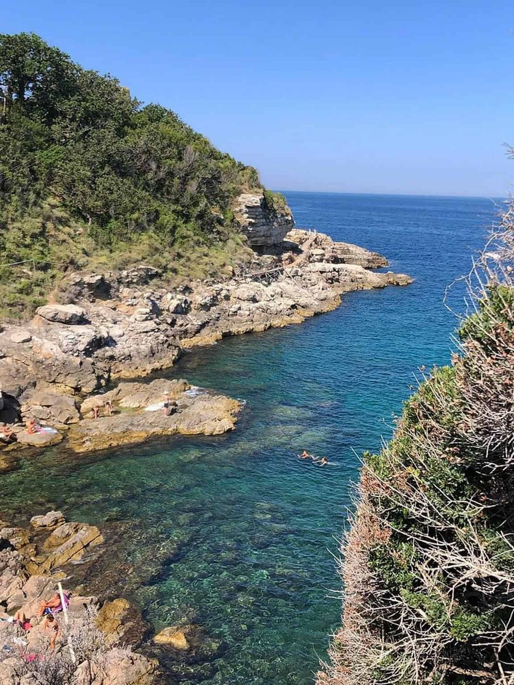 Serene coastal cove with rocky shoreline, lush greenery, and turquoise waters perfect for swimming and relaxing.