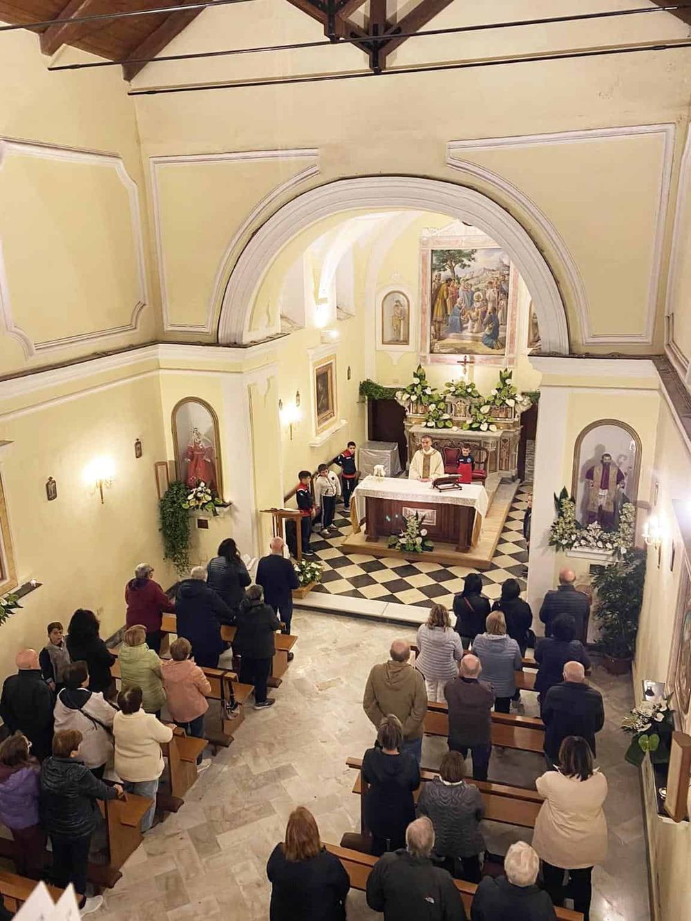People gathered inside a church for a religious service, with altar and religious artwork visible.