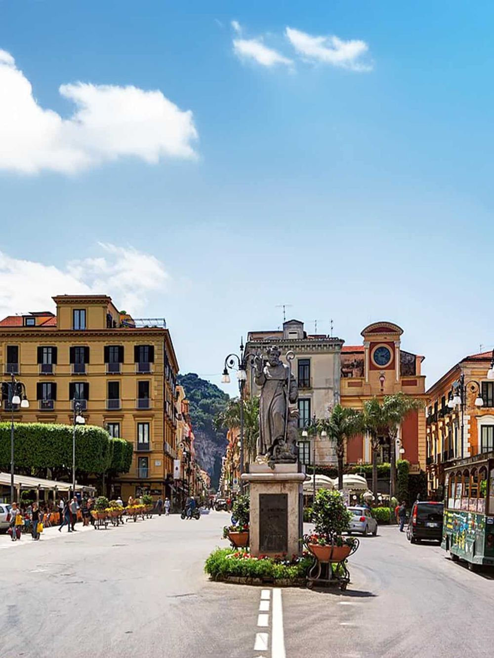 Colorful European city street with historic architecture, statues, and lively atmosphere.