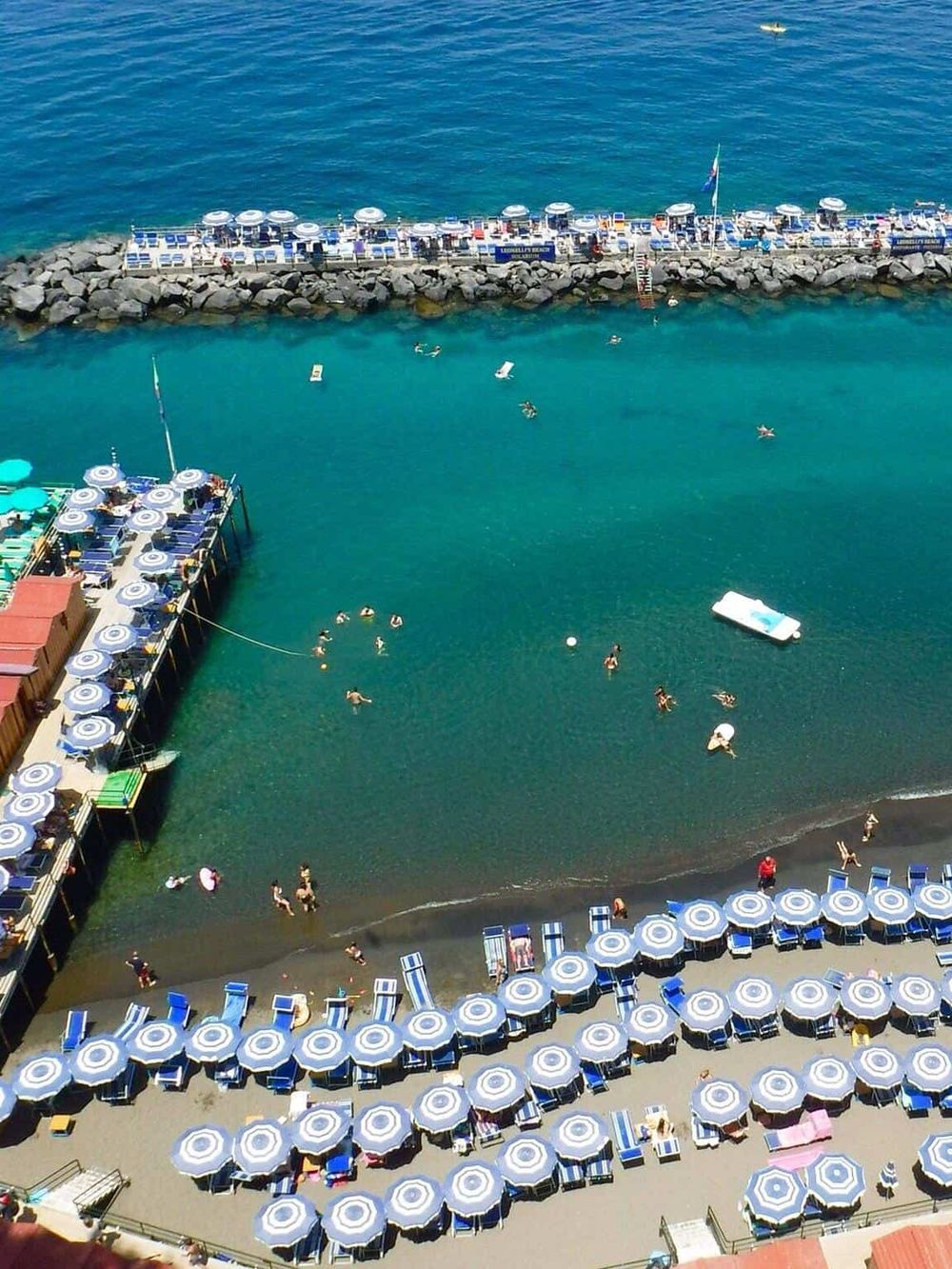 Colorful beach scene with umbrellas, sunbathers, and swimmers near the pier at Longport Beach.