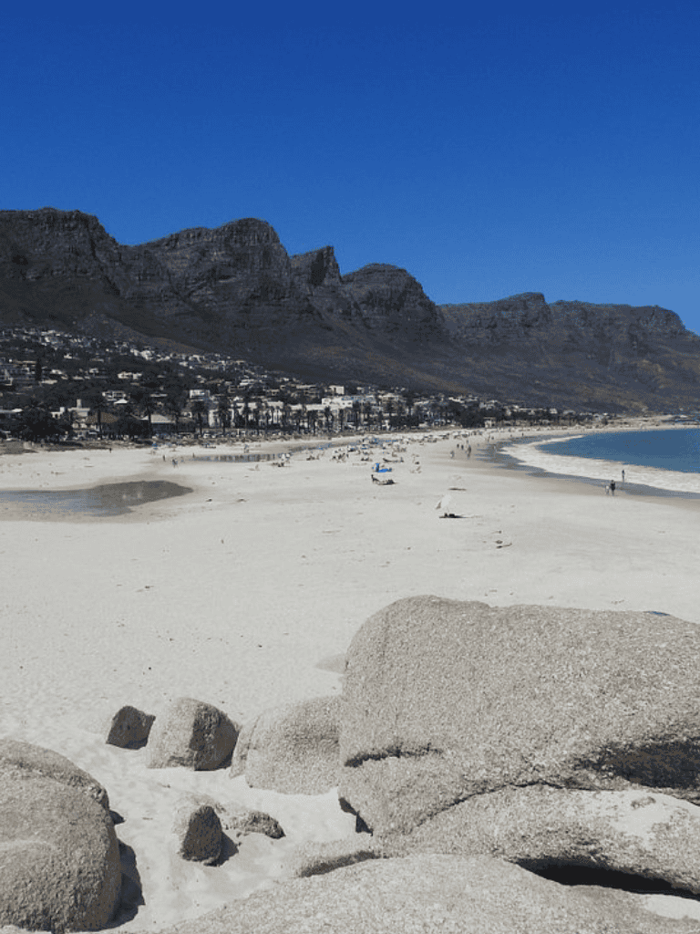 Sunny beach with granite rocks and mountain backdrop, perfect for travel and outdoor adventures.