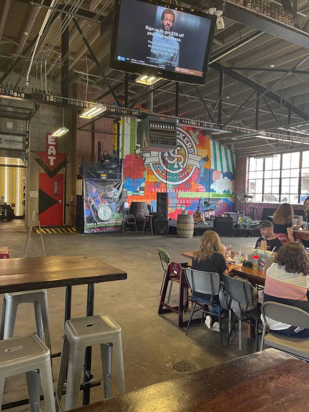 Vibrant indoor brewery with live music, colorful wall art, and casual seating for socializing and entertainment.
