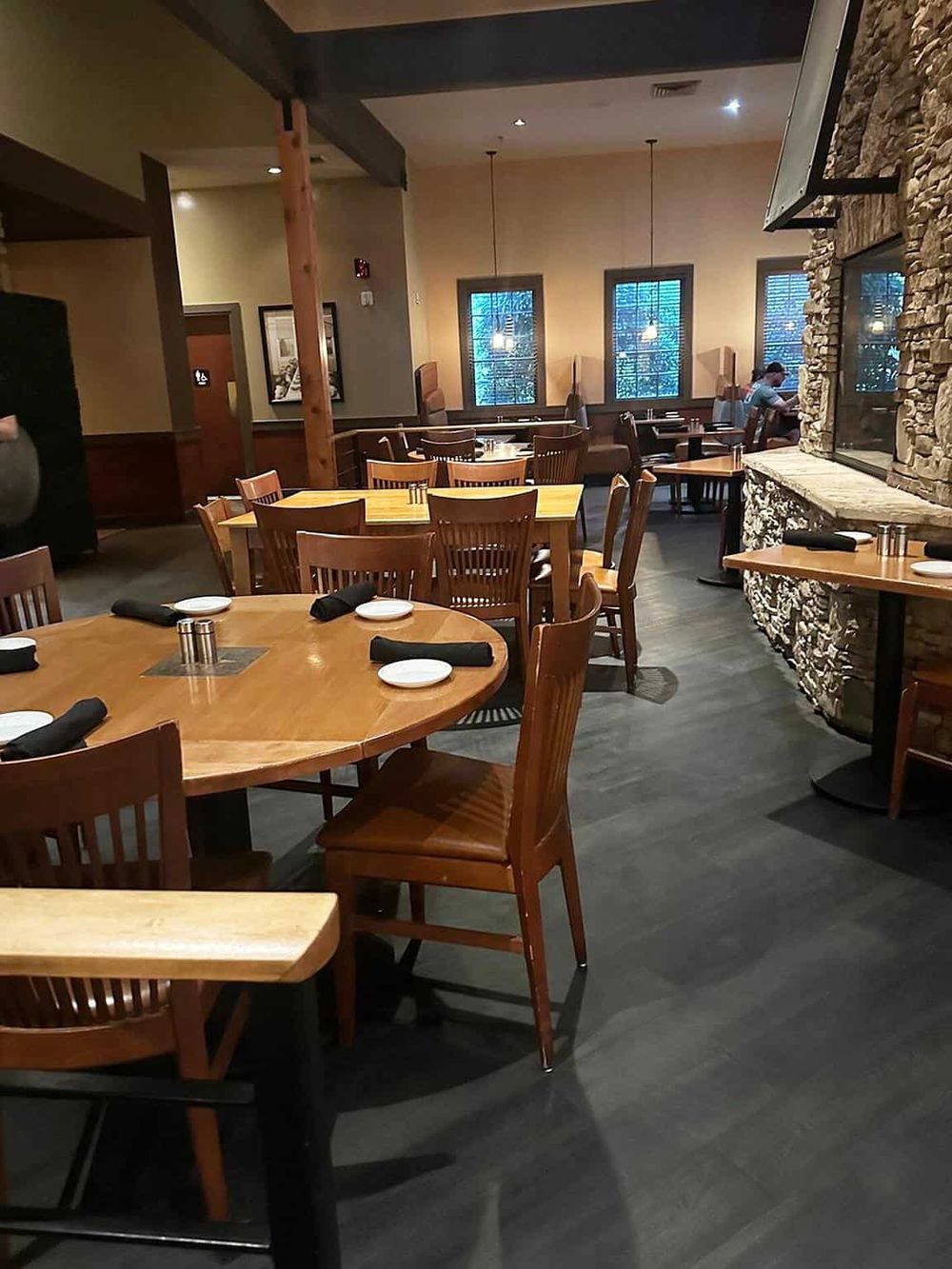 Cozy modern restaurant interior with wooden tables, stone fireplace, and ambient lighting for dining experience.