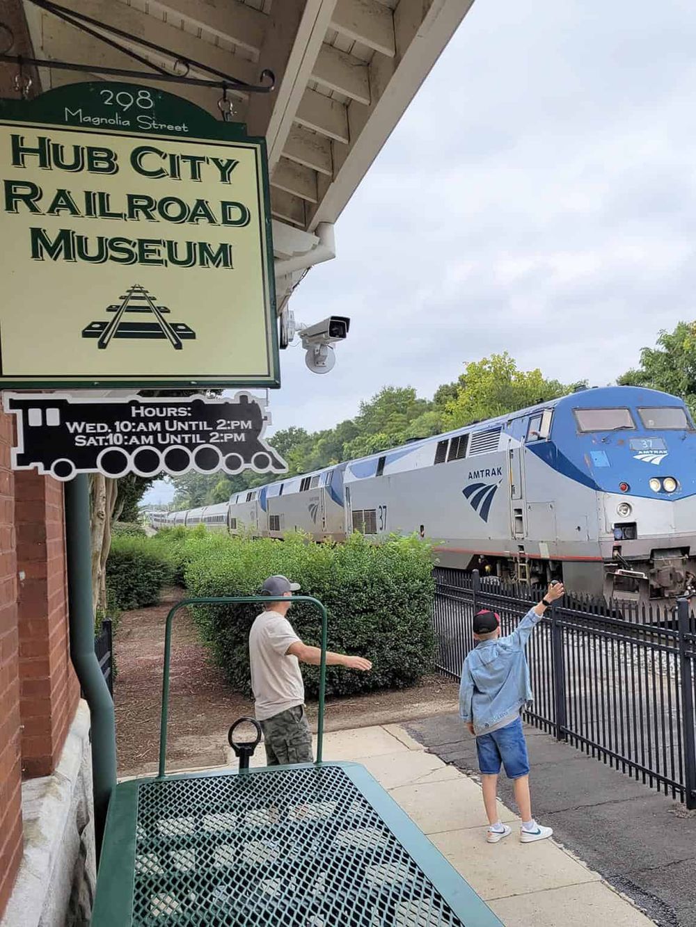 Classic Amtrak train passing by at Hub City Railroad Museum, with visitors enjoying the scenic view.