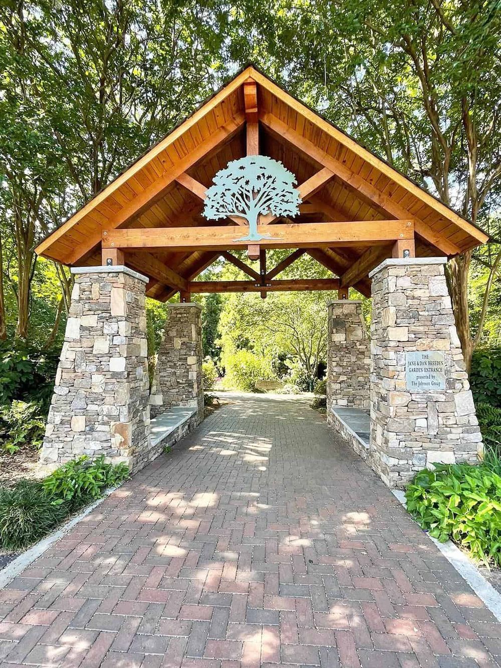 Serene garden entrance with stone pillars and wooden roof, featuring a decorative tree emblem for tranquility.
