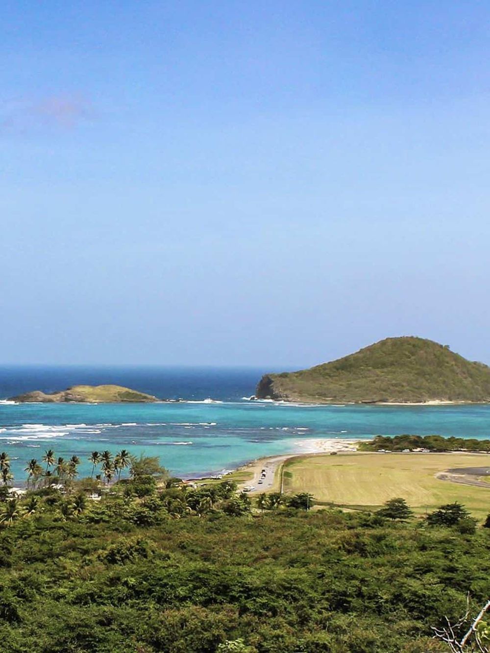 Stunning tropical island view with turquoise waters, lush greenery, and distant hills, perfect for travel and vacation planning.