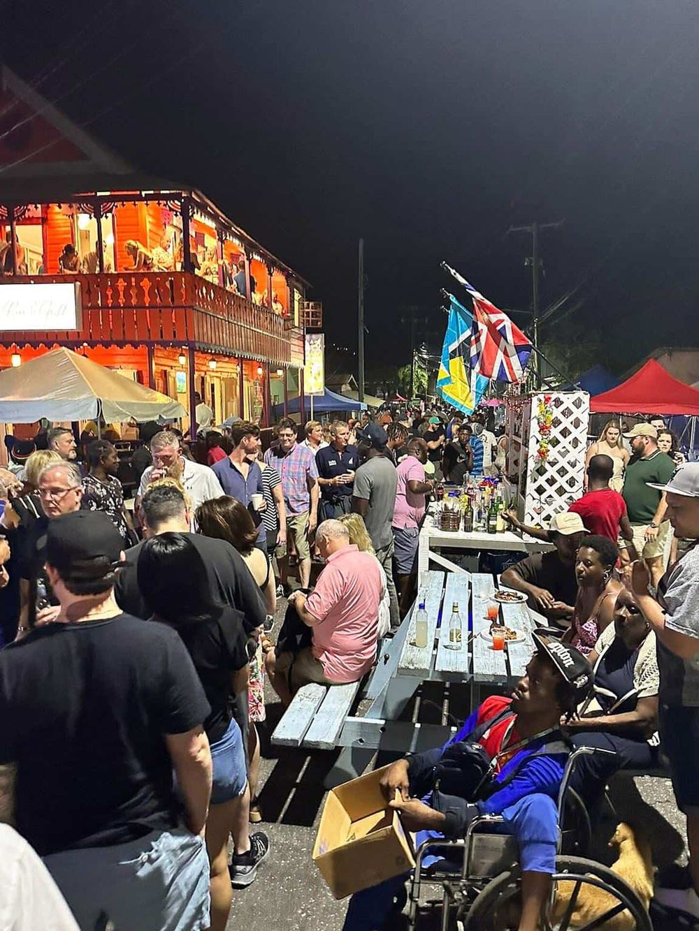 Vibrant street festival at night with diverse crowd, food stalls, flags, and lively atmosphere.