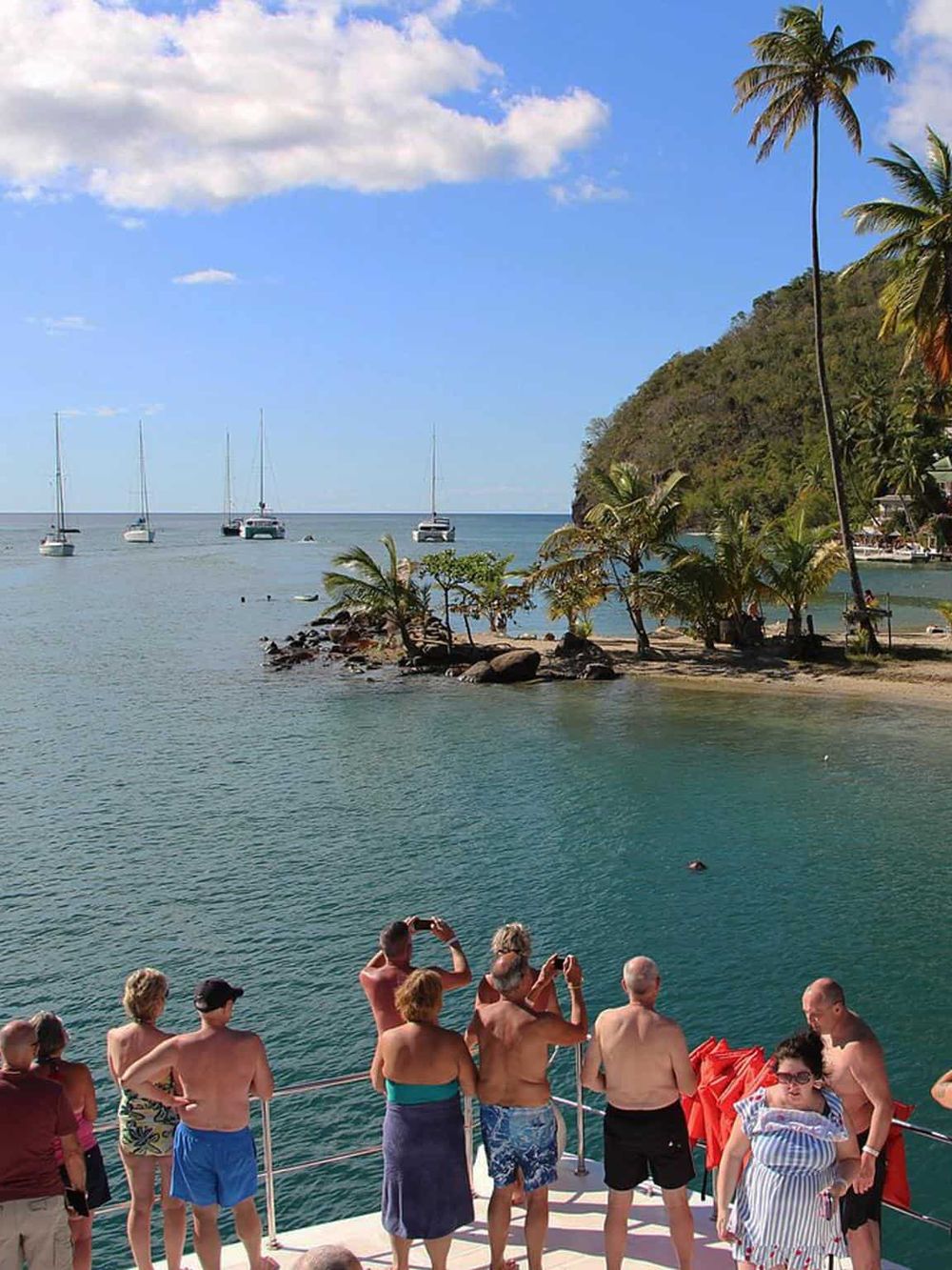 Relaxing tropical beach with palm trees, sailboats, and tourists enjoying scenic ocean views.