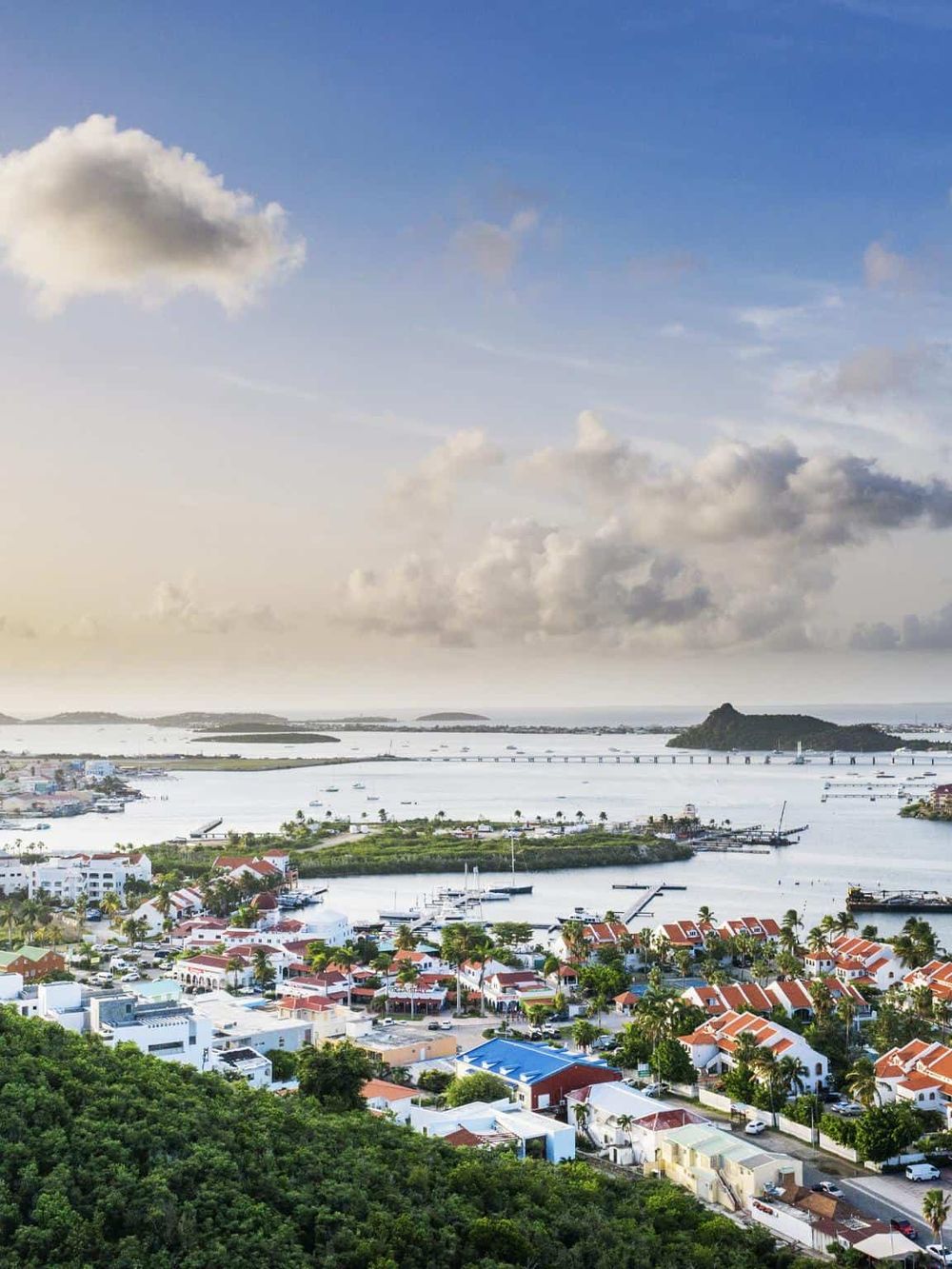 Colorful coastal town with waterway, bridges, and lush green landscape in the background.
