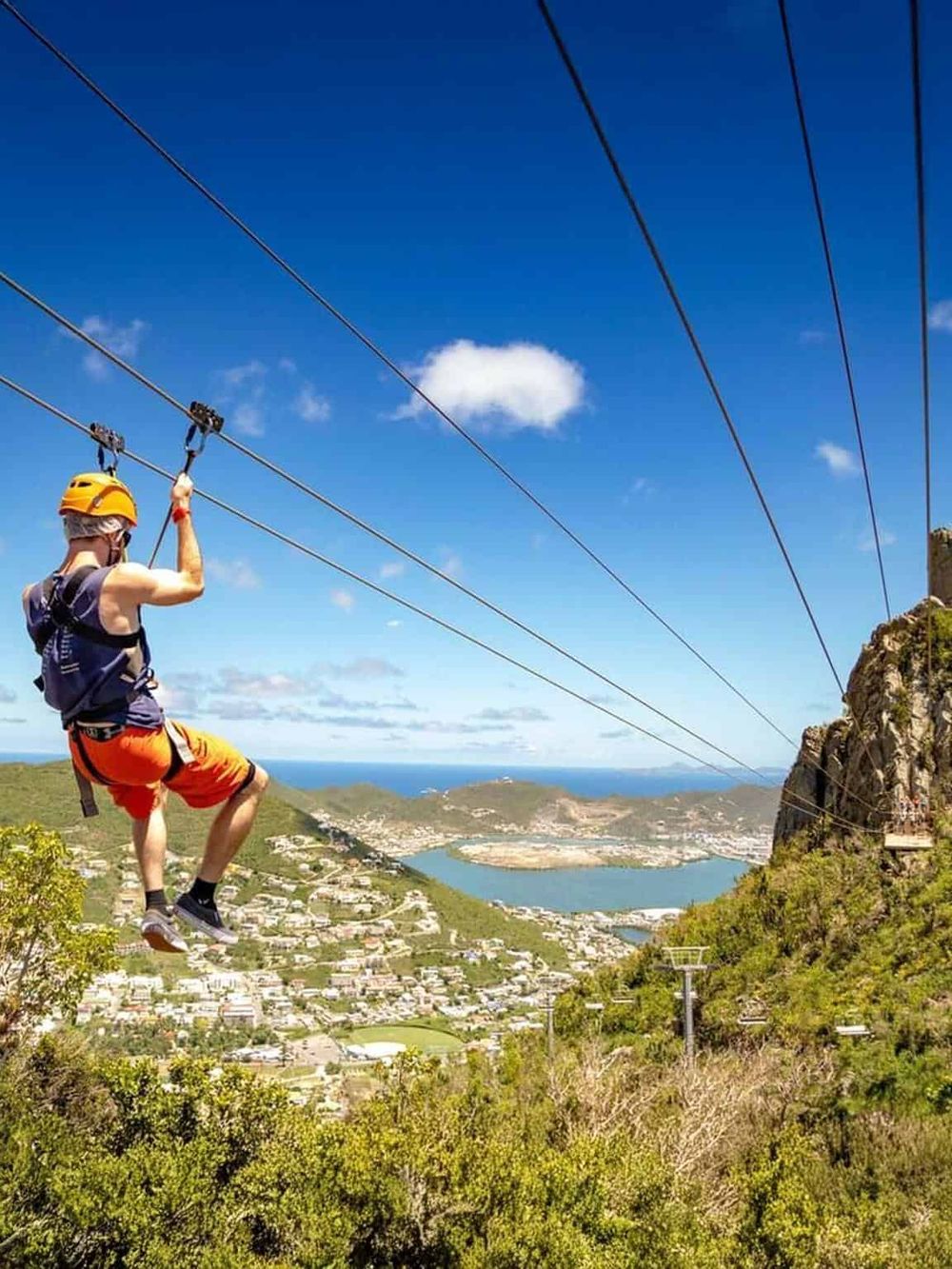 Thrill-seeker ziplining over scenic landscape with lake, mountains, and blue sky. Adventure, outdoor activity, and aerial tour experience.