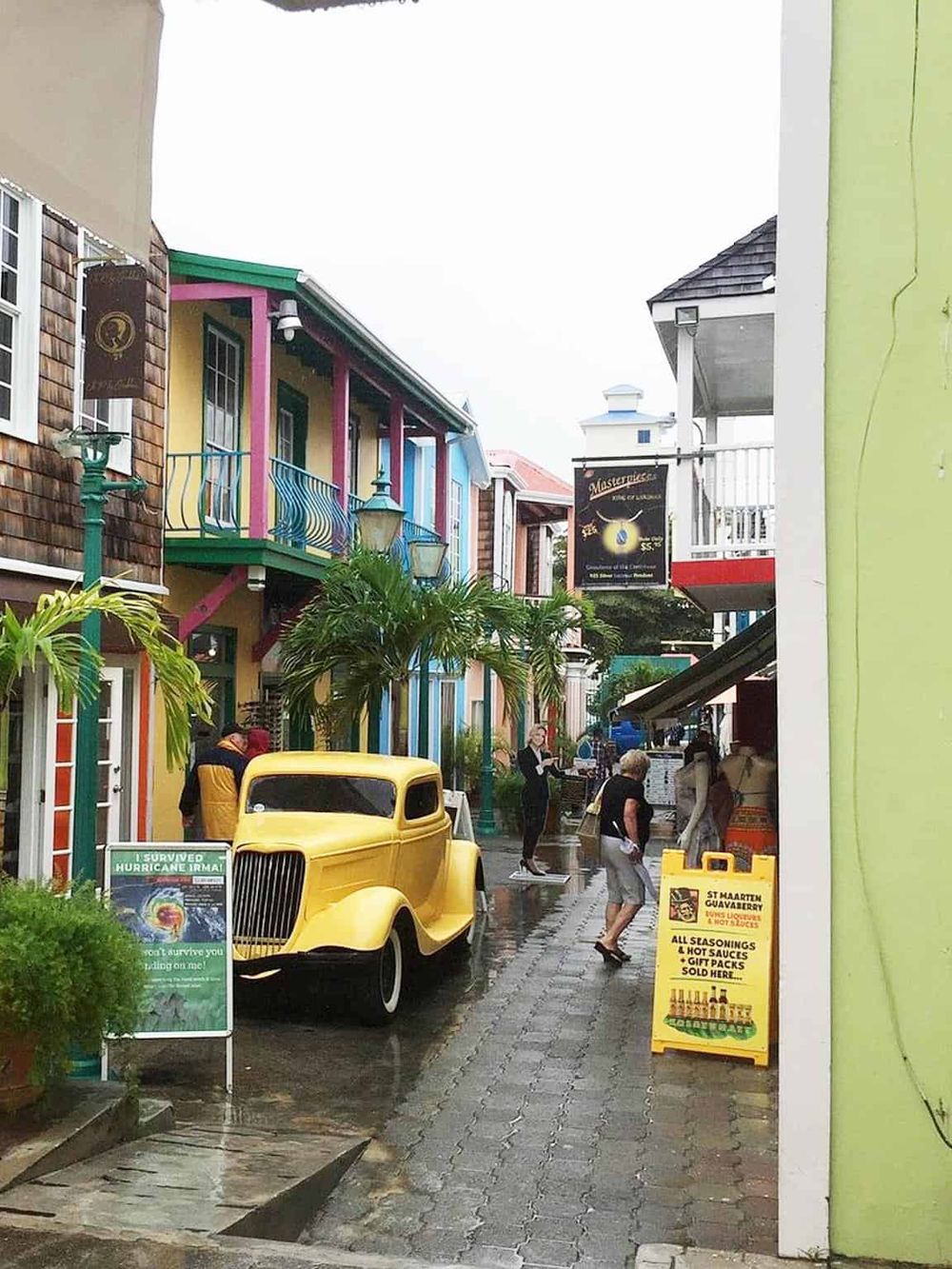 Colorful Caribbean street scene with vintage car, shops, and wet pavement, lively and vibrant, perfect for exploring Bemuda.