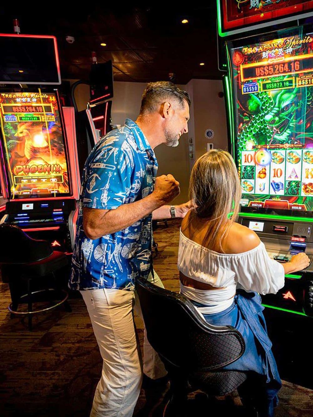 Exciting casino scene with two people playing slot machines in a lively, brightly lit gaming environment.