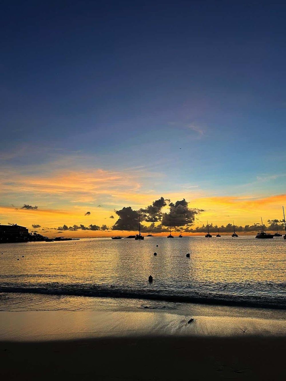 Stunning sunset over a calm ocean with sailboats, colorful sky, and tranquil beach scene.