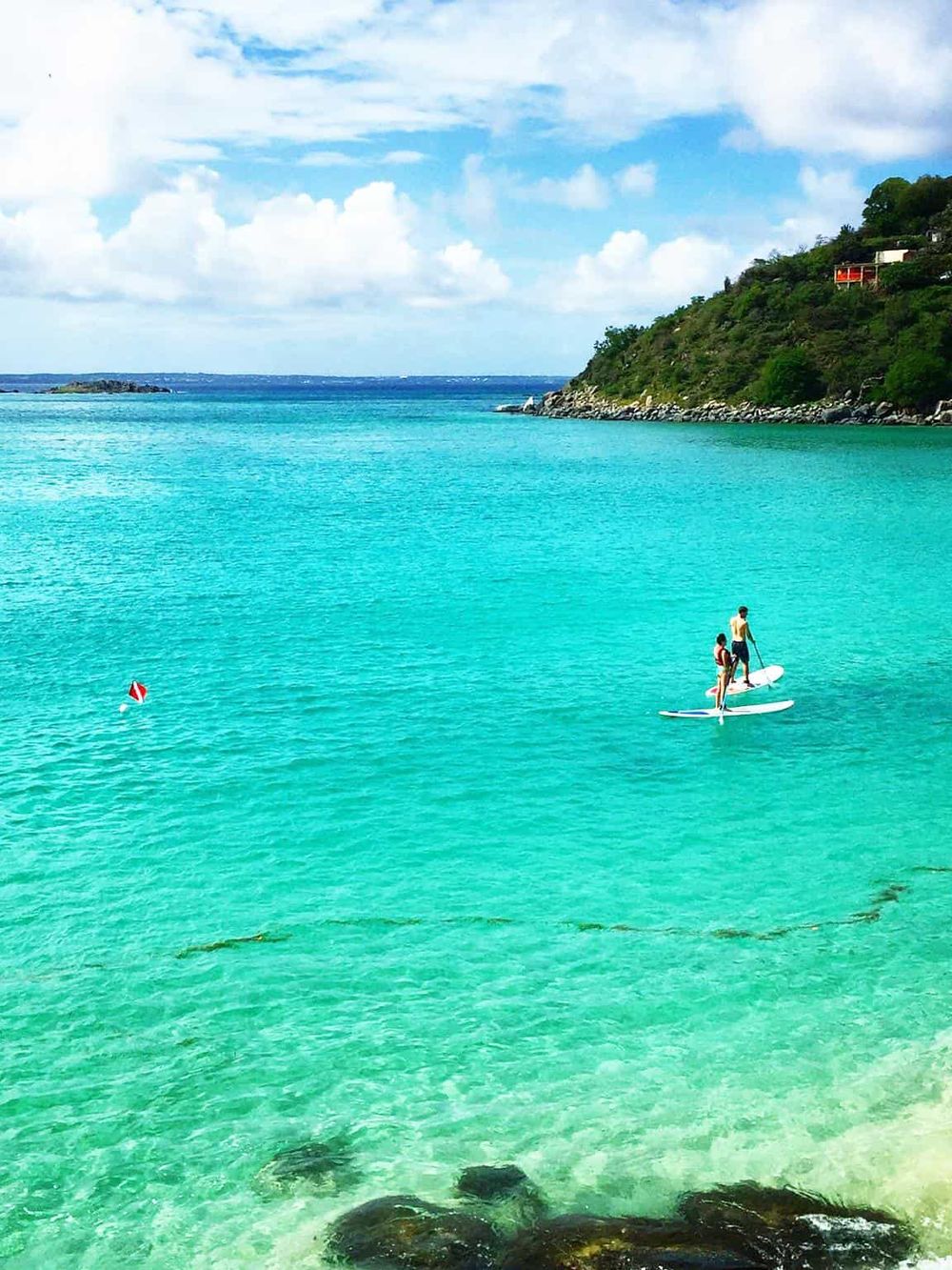 Bright turquoise ocean with paddleboarders, lush green hills, and blue sky - perfect for travel and adventure.