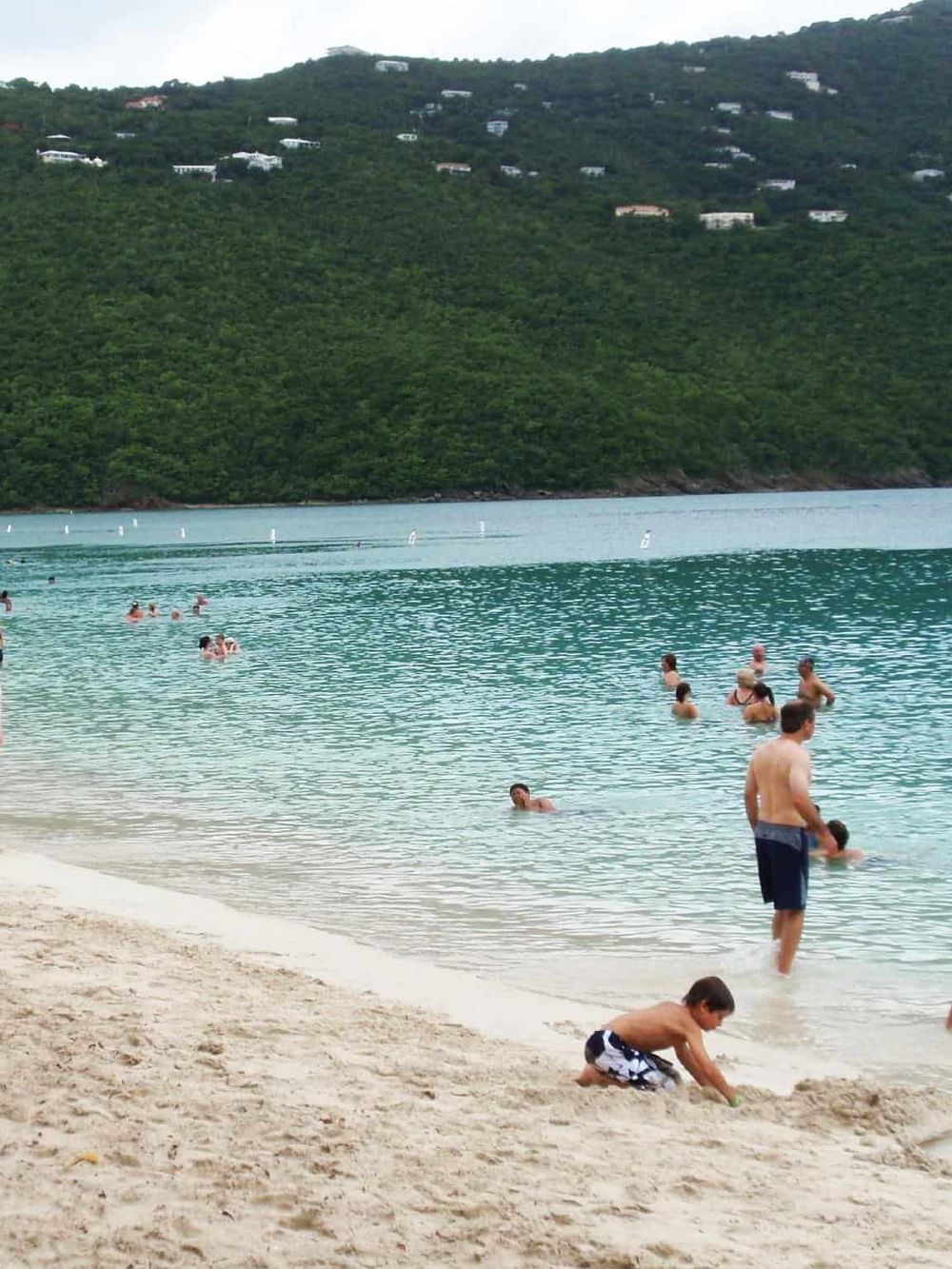 Kids playing at the beach with turquoise water and a lush green hillside in the background.