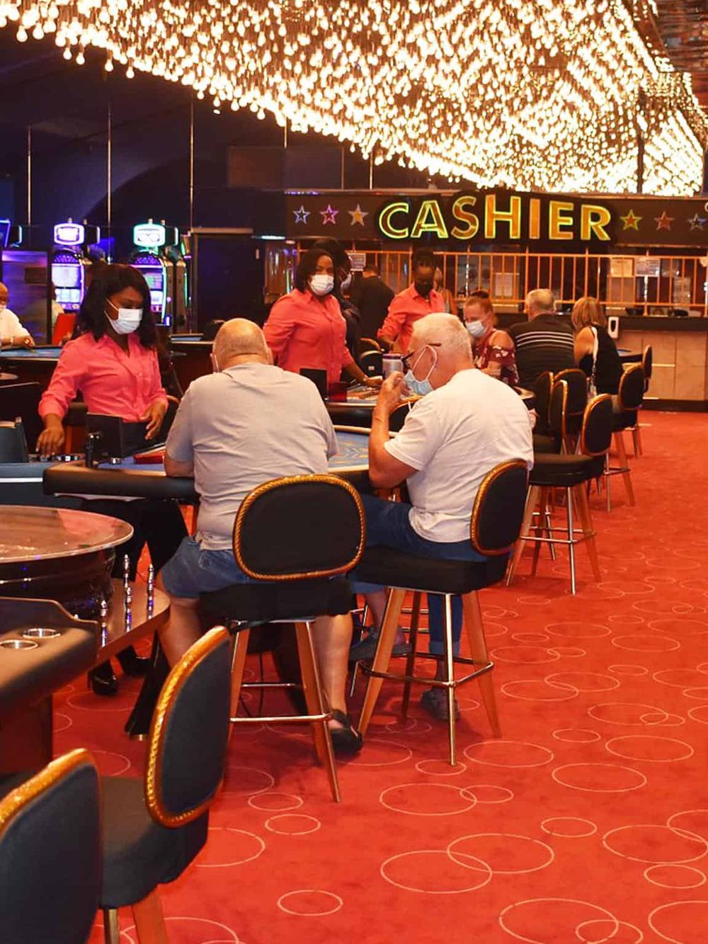 Smiling group playing poker at casino table with "Cashier" sign in background.