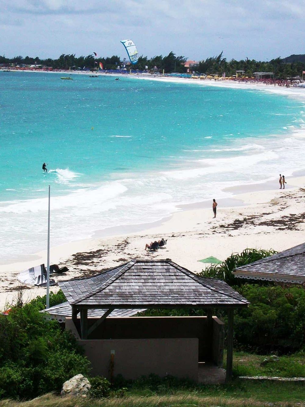 Vibrant beach scene with turquoise ocean, kite surfers, and sandy shoreline at a tropical destination.