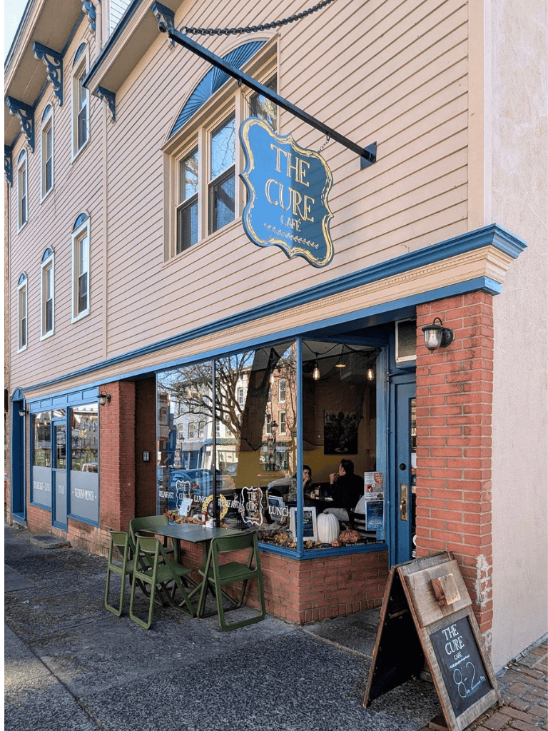 Cozy café exterior with outdoor seating and large window, located in a charming neighborhood.
