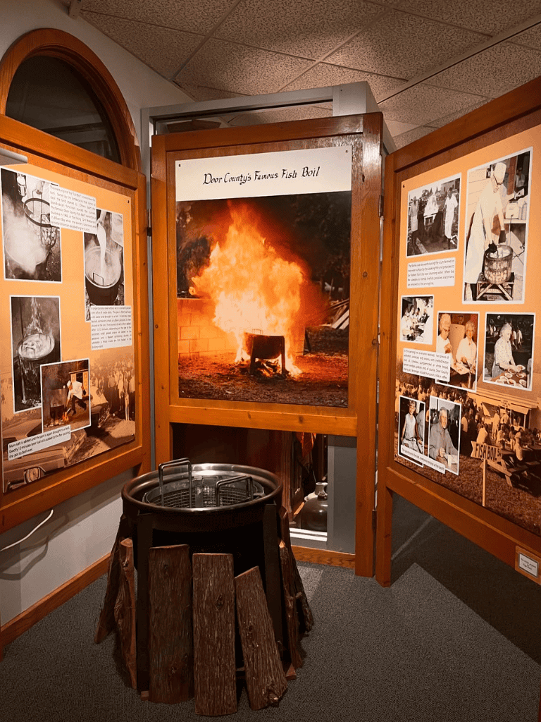 Large fire display at historic fish boil event with informative informational boards about local traditions.