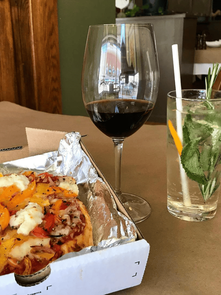 1. Wine glass with red wine, pizza box, and cocktail with mint on restaurant table.