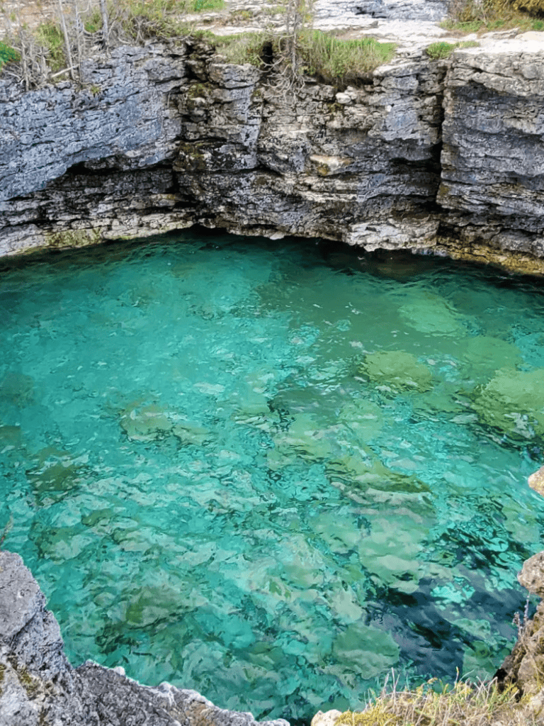 Pristine turquoise spring water surrounded by rocky cliffs, located in a scenic outdoor nature setting.