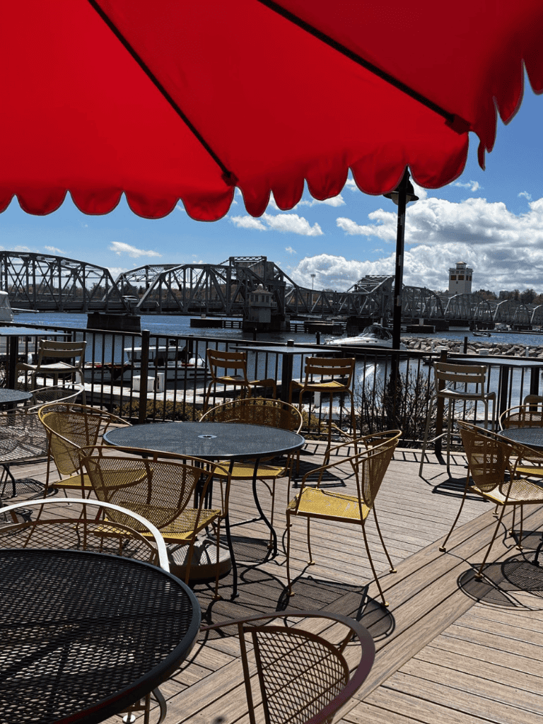 Outdoor waterfront dining with bridge views and red umbrella in the foreground.