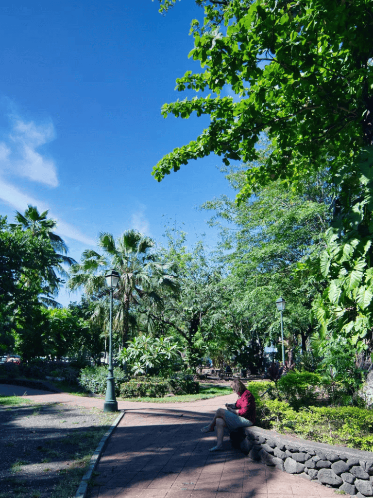 Serene park with lush green trees and a person sitting on a bench under bright blue sky.