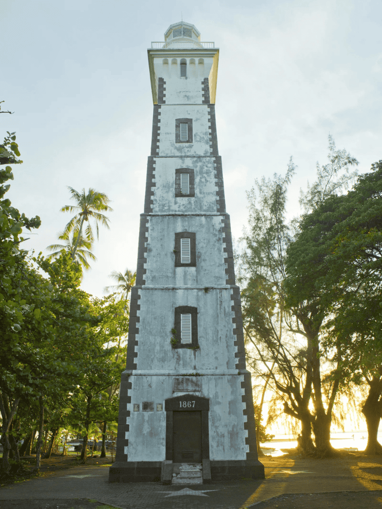Stone lighthouse with date 1867, surrounded by tropical trees, sunny evening, historic navigation landmark, QuestForDirections.