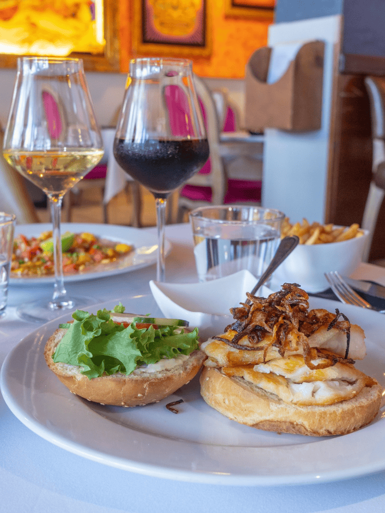 Juicy burger with crispy fried onions and fresh greens served with wine and fries at Quest For Directions.