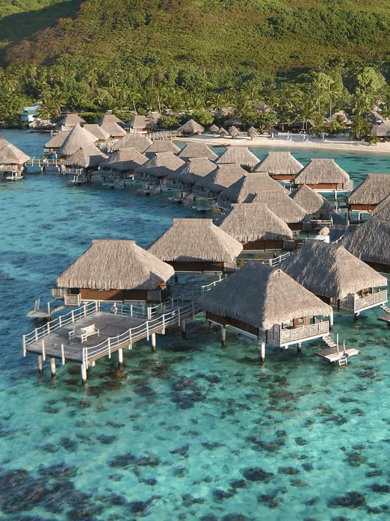 Overwater bungalows at a tropical island resort with crystal-clear water and lush greenery in the background.