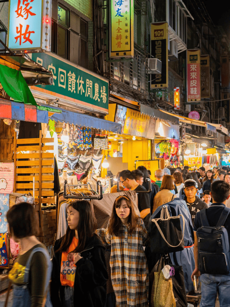 Crowded night market in Taiwan with vibrant lights, street vendors, and diverse shoppers.