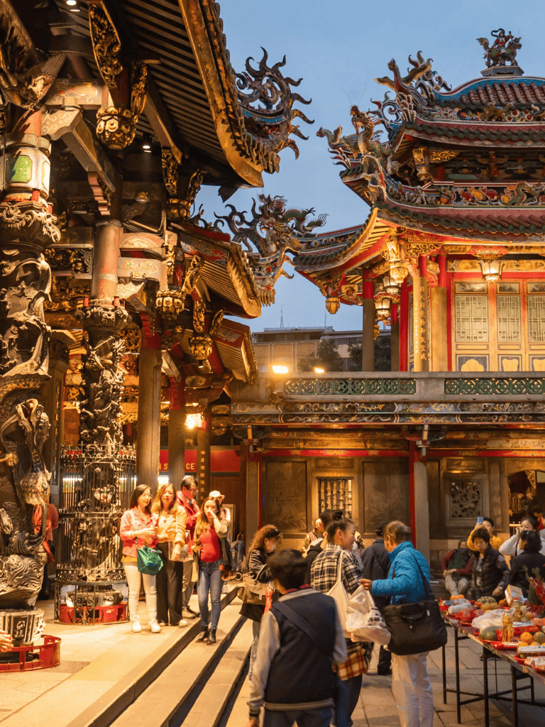 Colorful traditional Chinese temple with visitors shopping and exploring at dusk.