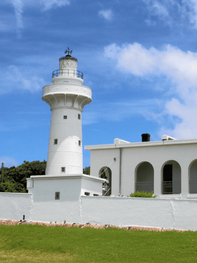 White lighthouse and building at coastal location, scenic sky background.