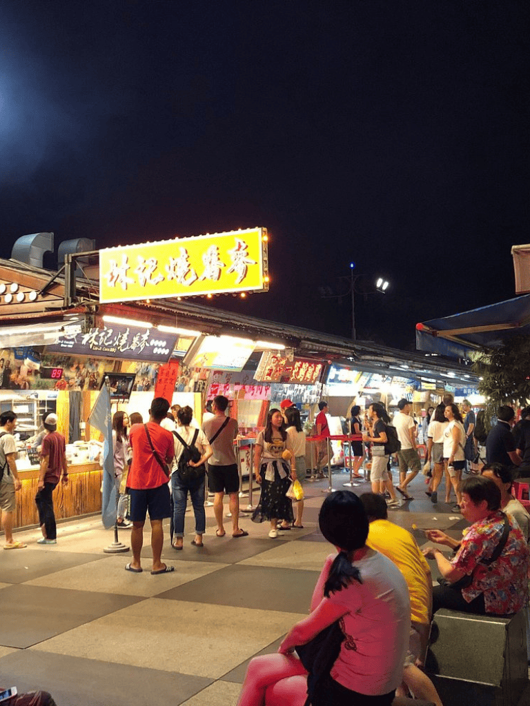 Bright night market scene at QuestForDirections food stalls in Taiwan, lively crowd, vibrant lights, authentic street food experience.