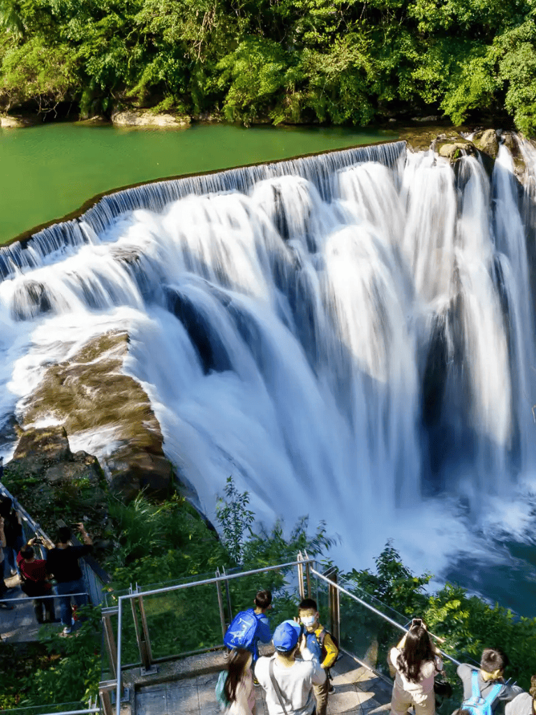 Vibrant waterfall scene at QuestForDirections, featuring lush greenery and tourists enjoying the view.