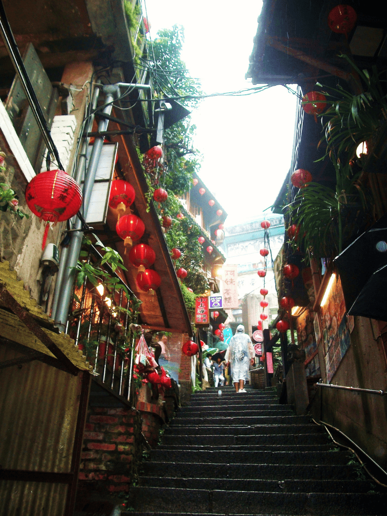 Red lanterns decorate lively street stairs in Chinatown with shops and tourists.