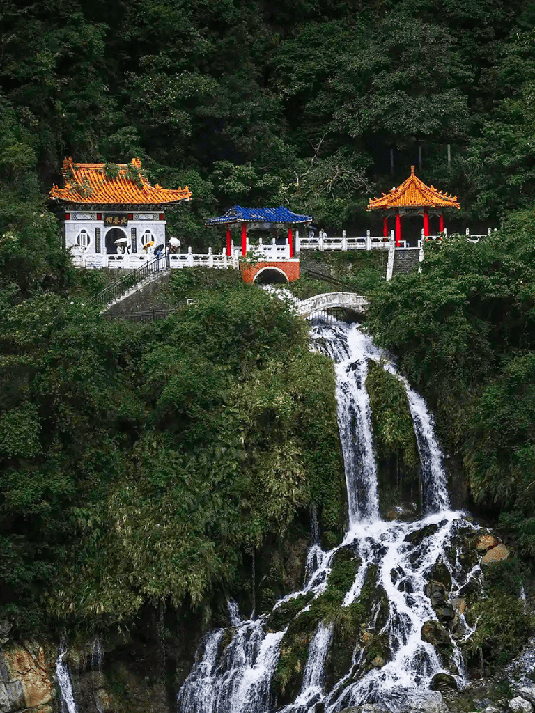 Traditional Chinese temple overlooking a cascading waterfall surrounded by lush greenery.