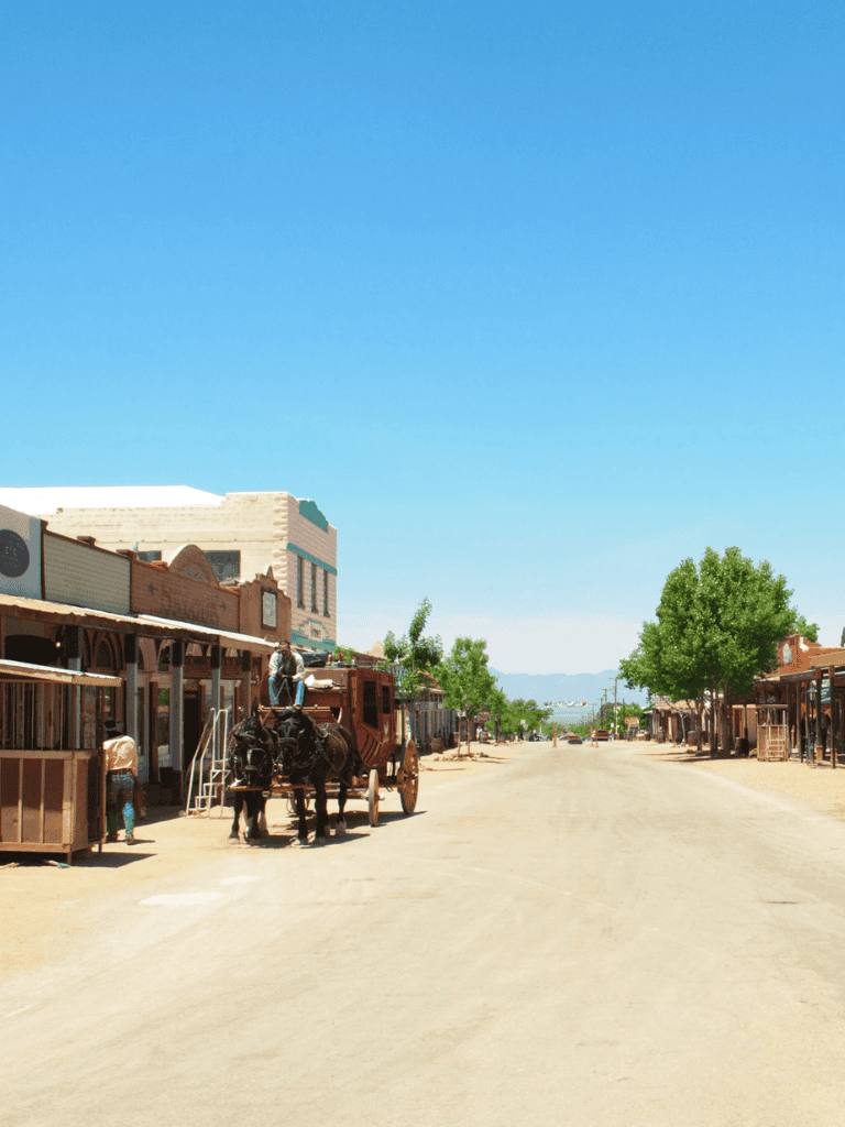 Old West town street with wooden storefronts, horse-drawn carriage, and clear blue sky, highlighting travel and adventure.
