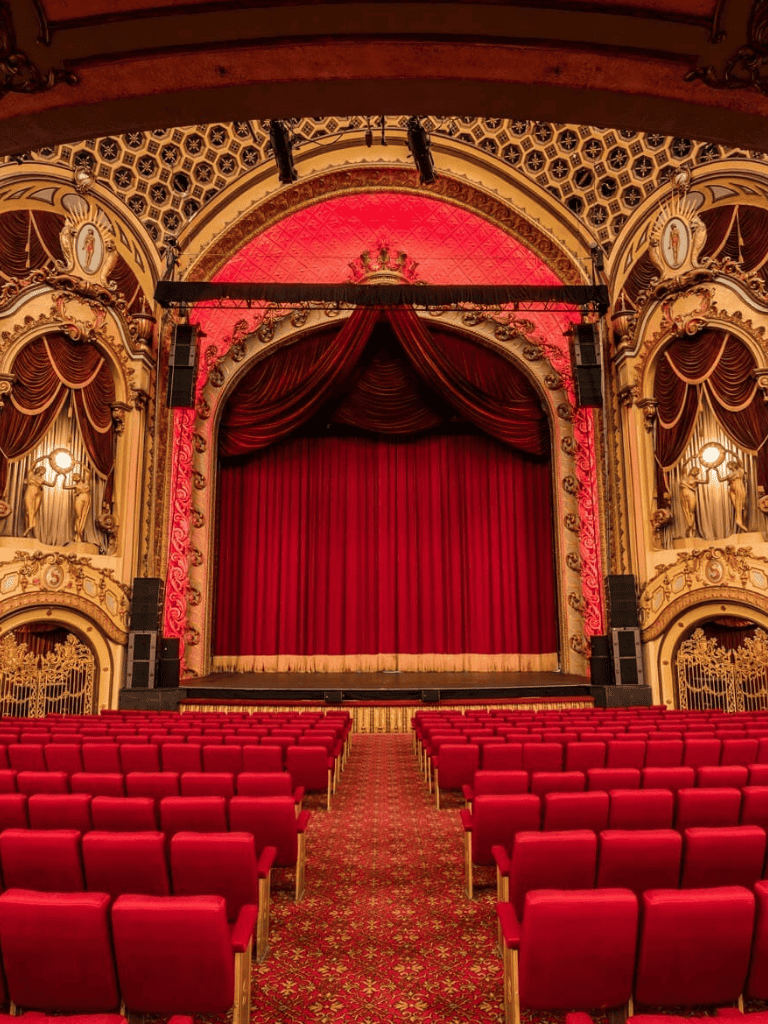 Luxurious theater interior with ornate gold detailing and plush red velvet curtains.
