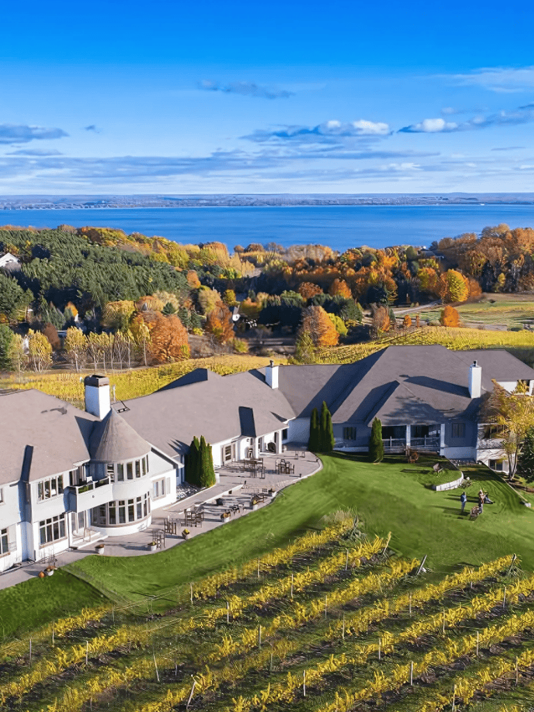 Scenic lakeside property with vineyard, lush landscaping, and stunning water views in autumn.