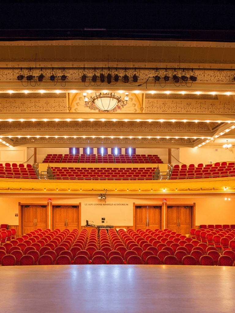 Ornate theater auditorium with red velvet seats and decorative ceiling lighting, ideal for performances or events.