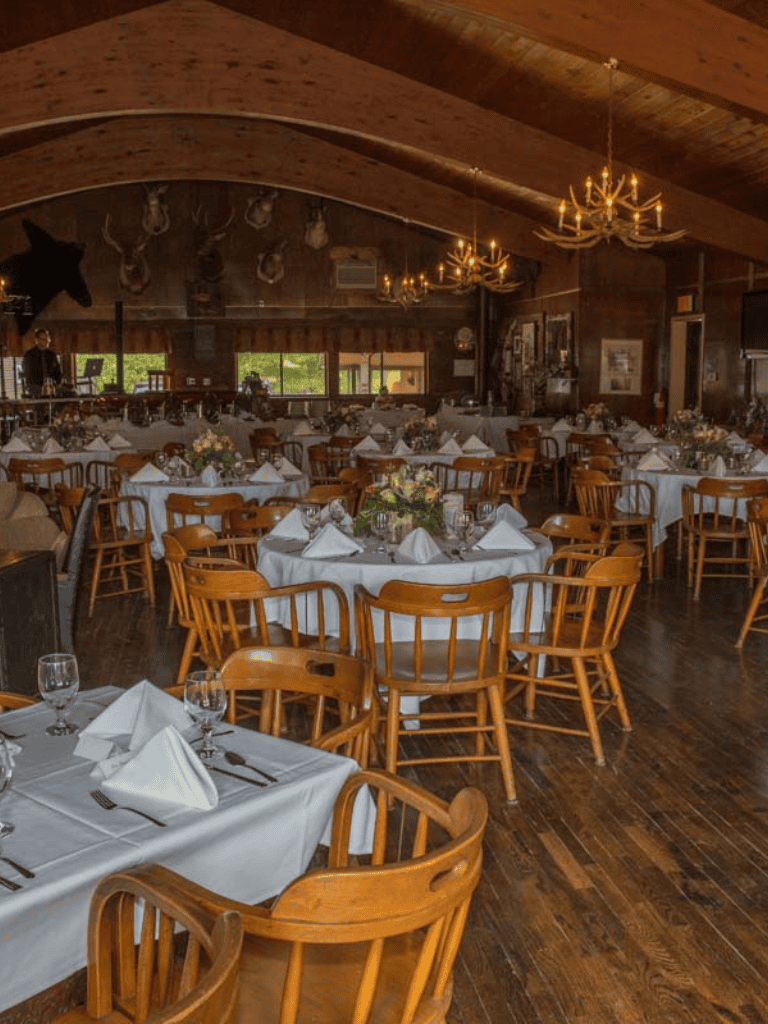 Cozy rustic restaurant decorated with chandeliers and mounted animal heads, set for a formal dinner.