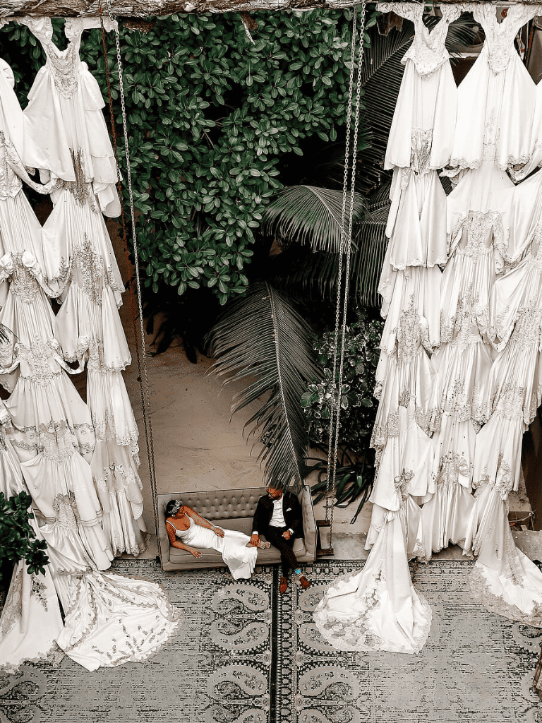 Elegant outdoor wedding setup with white floral drapes and lush greenery background.