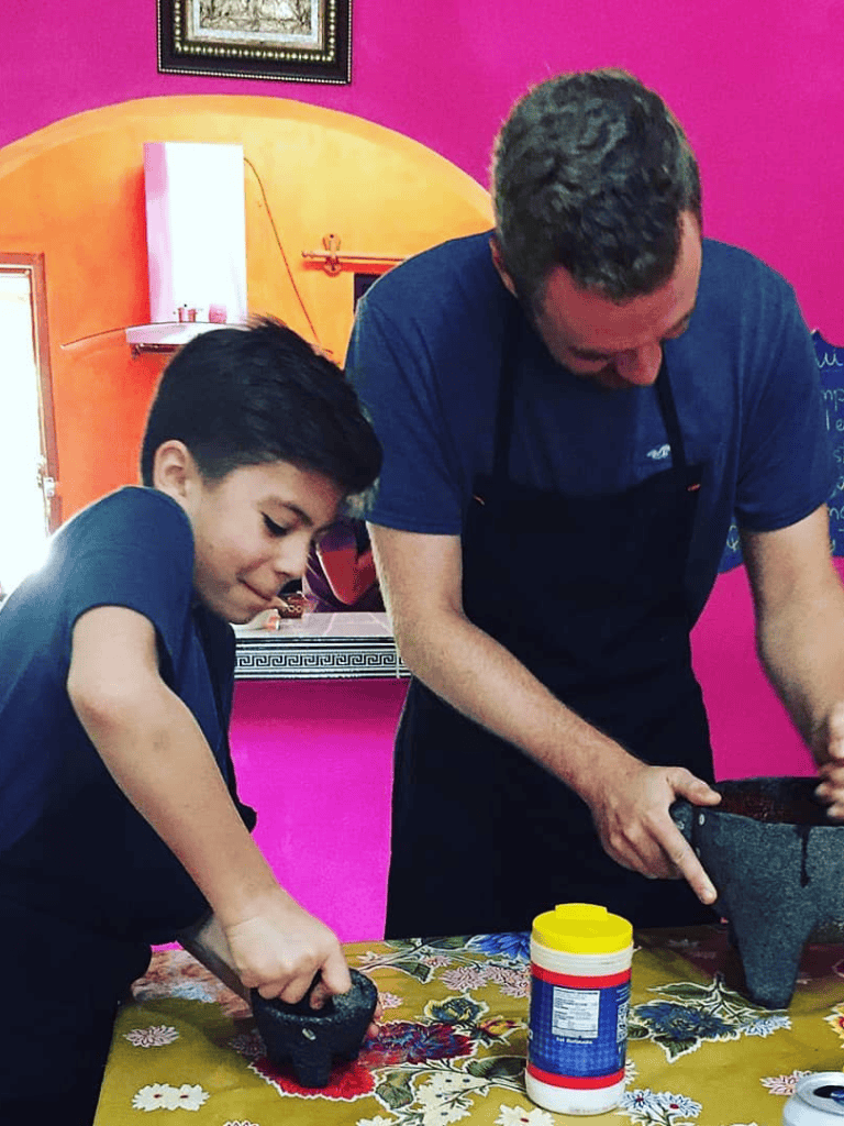 Rubbing mortar with a young boy and adult in a colorful kitchen, demonstrating a fun cooking activity.