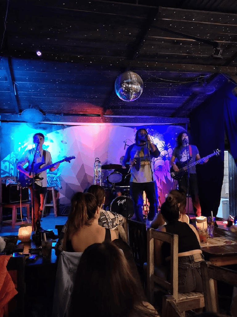 Live music band performing at a cozy venue with colorful stage lighting and disco ball, entertaining an engaged audience.