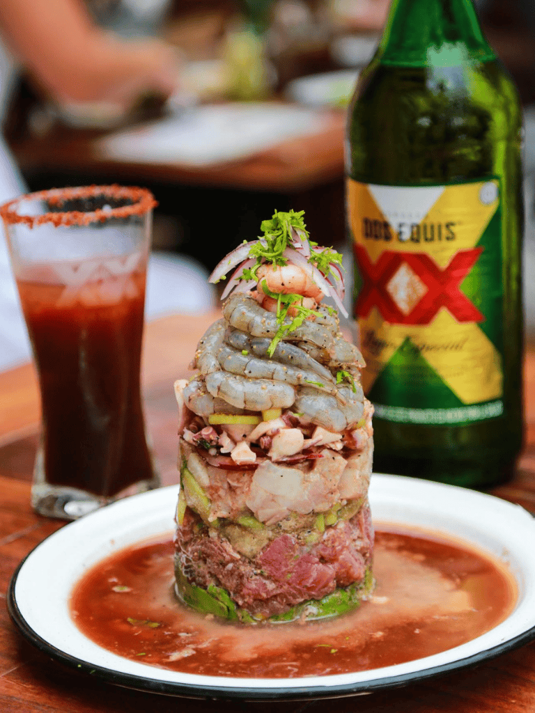 Raw seafood tower with shrimp and fish, served with sauce, beer, and a spicy drink.
