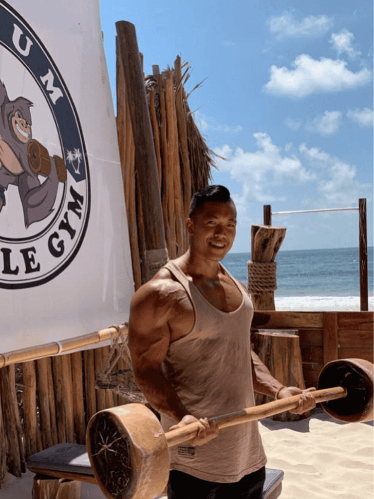 Strongman at beach gym holding wooden barbell for strength training and fitness.